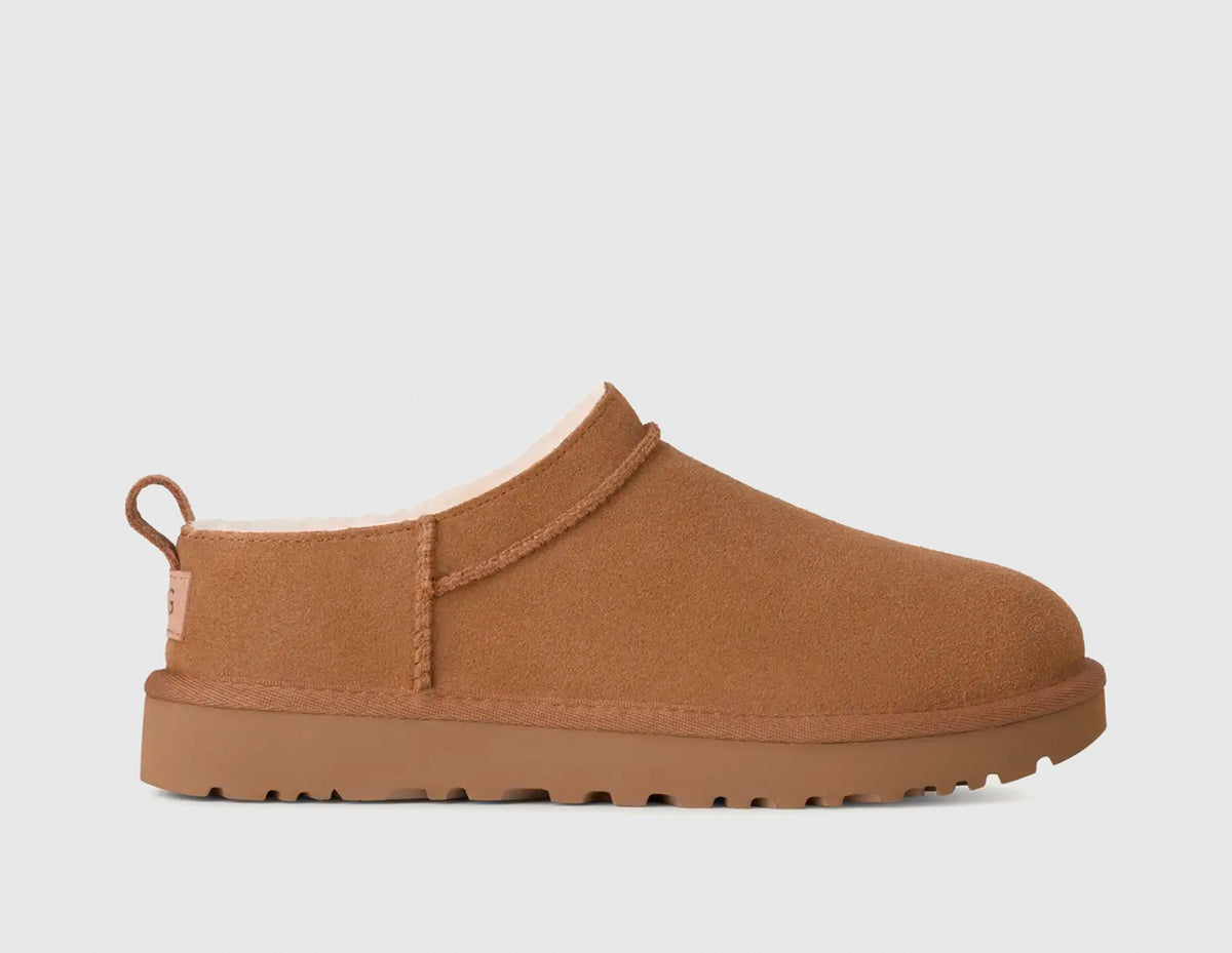 UGG Women's Classic Micro. Side view of chestnut suede mini boots featuring overlock stitch seams, heel pull tab, shearling lining, and matching treaded foam outsole. 