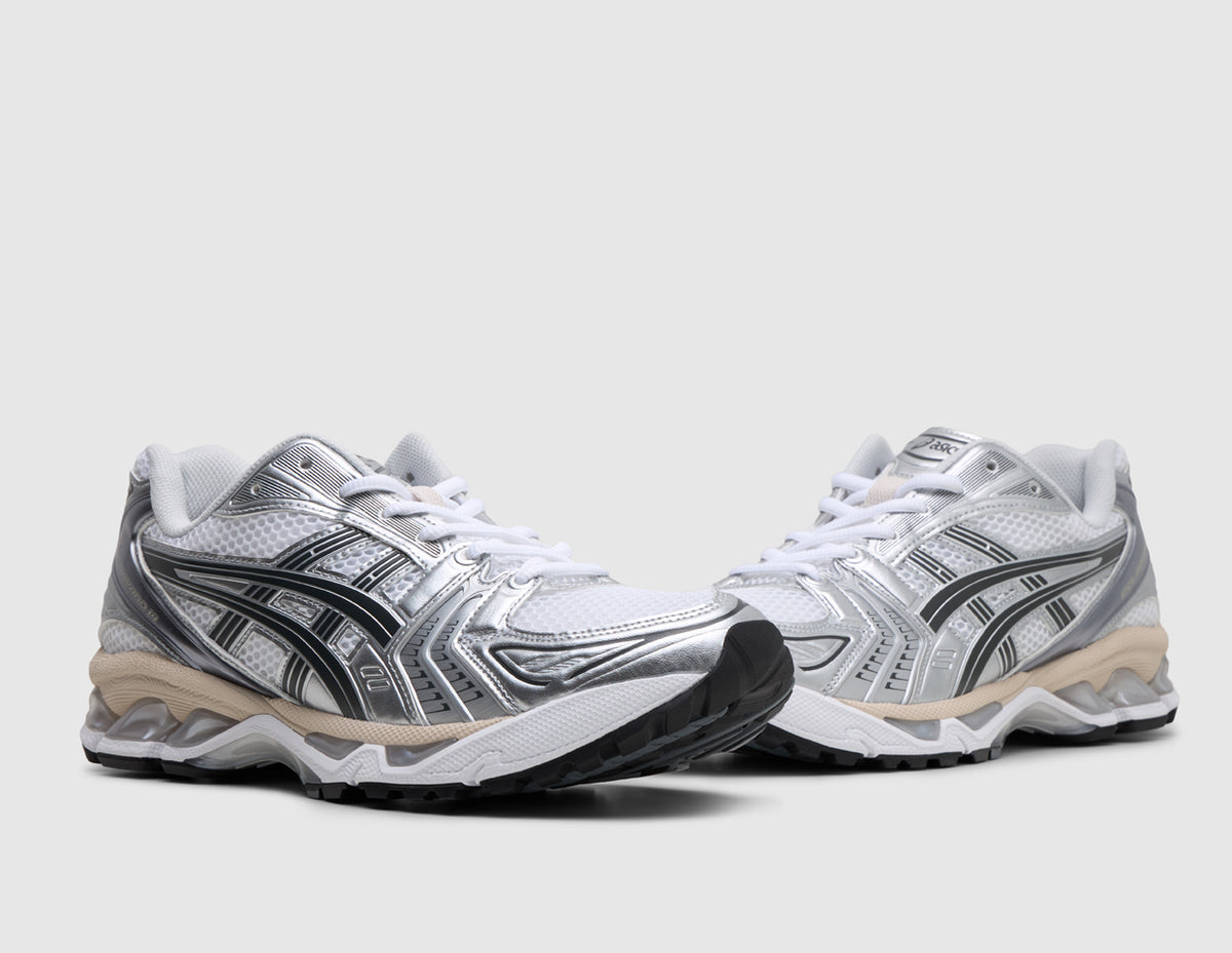 ASICS GEL-KAYANO 14. Three-quarter view of pair of white running shoes showing metallic silver and graphite grey overlays, white laces, and cushioned midsole. 