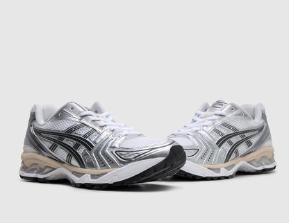 ASICS GEL-KAYANO 14. Three-quarter view of pair of white running shoes showing metallic silver and graphite grey overlays, white laces, and cushioned midsole. 