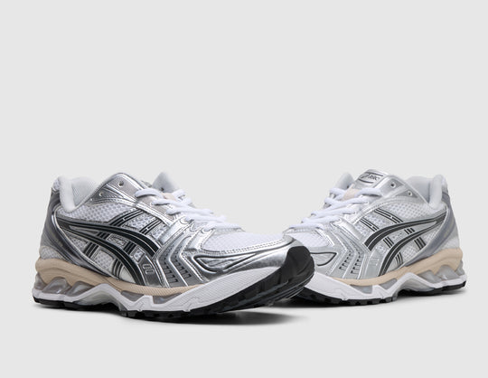 ASICS GEL-KAYANO 14. Three-quarter view of pair of white running shoes showing metallic silver and graphite grey overlays, white laces, and cushioned midsole. 