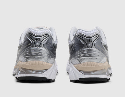 ASICS GEL-KAYANO 14. Rear view of pair of white running shoes showing metallic silver heel counters, beige heel accents, and dark rubber outsole pods. 