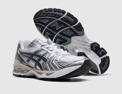 ASICS GEL-KAYANO 14. Three-quarter view of white running shoes with one shoe propped up to display the dark rubber traction outsole. 