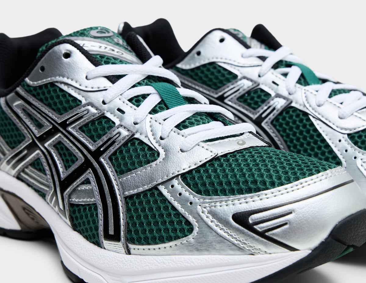 ASICS GEL-1130. Close-up three-quarter view of forefoot showing evergreen mesh toe box, metallic silver overlays, white eyestays with white laces, and tongue with ASICS logo patch. 
