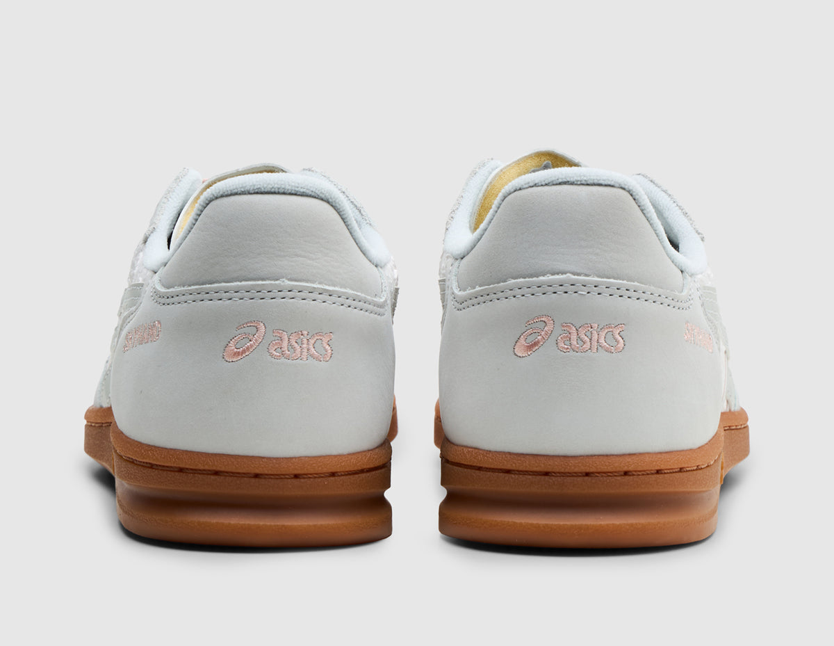 ASICS SKYHAND OG. Rear view of pair of glacier grey leather sneakers showing smooth leather heel overlays with blush pink embroidered ASICS logos and low-profile gum rubber midsoles. 