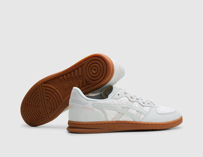 ASICS SKYHAND OG. Three-quarter view of glacier grey leather sneakers with one shoe turned to showcase the gum rubber outsole. 