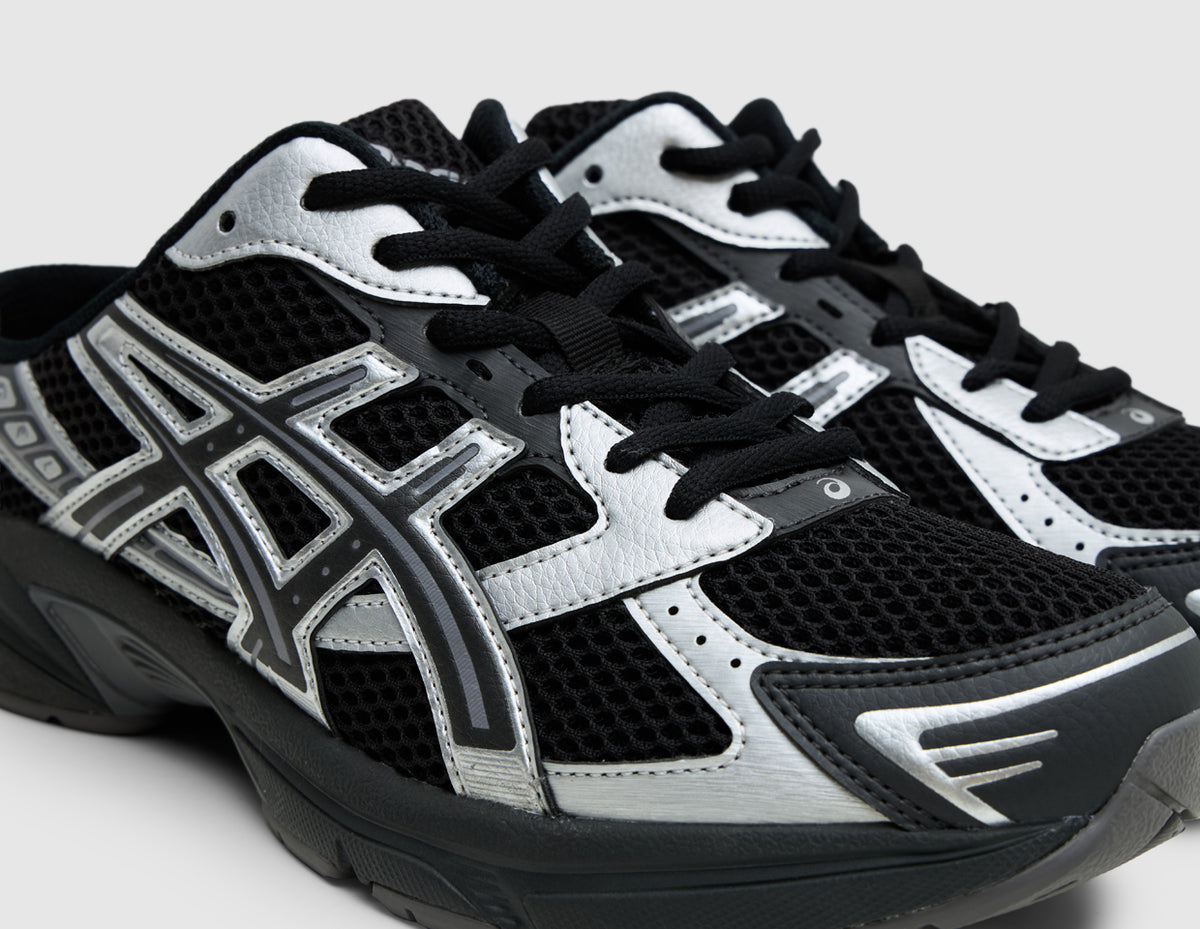 ASICS GEL-1130 Mule. Close-up three-quarter view of black mesh upper, black laces, and metallic graphite grey overlays. 