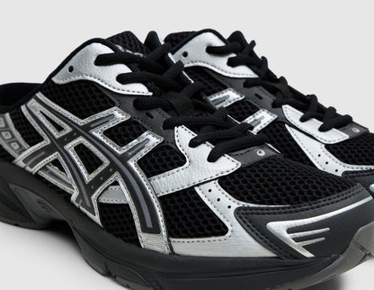ASICS GEL-1130 Mule. Close-up three-quarter view of black mesh upper, black laces, and metallic graphite grey overlays. 