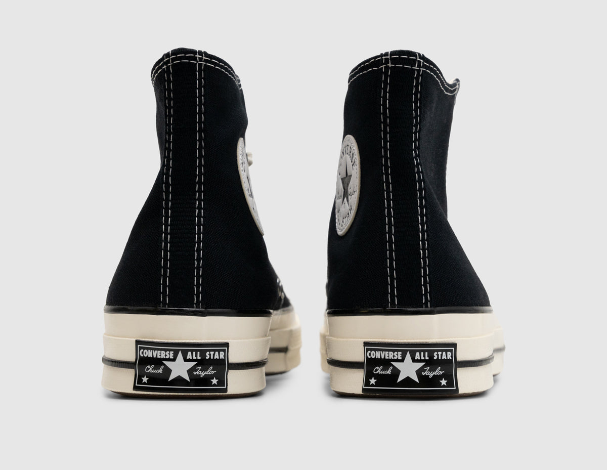 Converse Chuck 70 Hi. Rear view of pair of high-top sneakers showing black canvas heel strips, white contrast stitching, medial Chuck Taylor ankle patches, and glossy egret rubber midsoles with vintage black All Star license plate heel badges. 
