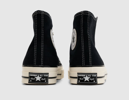 Converse Chuck 70 Hi. Rear view of pair of high-top sneakers showing black canvas heel strips, white contrast stitching, medial Chuck Taylor ankle patches, and glossy egret rubber midsoles with vintage black All Star license plate heel badges. 