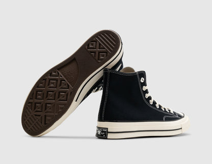Converse Chuck 70 Hi. Dynamic view of pair of high-top sneakers with one shoe turned to display the brown rubber tread outsole alongside the medial side of the shoe, highlighting the iconic Chuck Taylor All Star circular ankle patch. 