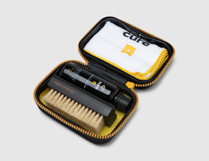 Crep Protect Travel Kit. Top view of open travel case showing cleaning solution bottle, wooden brush, and microfiber cloth. 