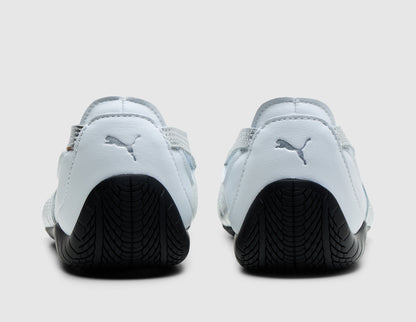 PUMA Women's Speedcat Nova. Rear view of pair of PUMA white ballet flat sneakers showing metallic silver PUMA Cat logos on heels and rounded black driver heel outsole extension. 