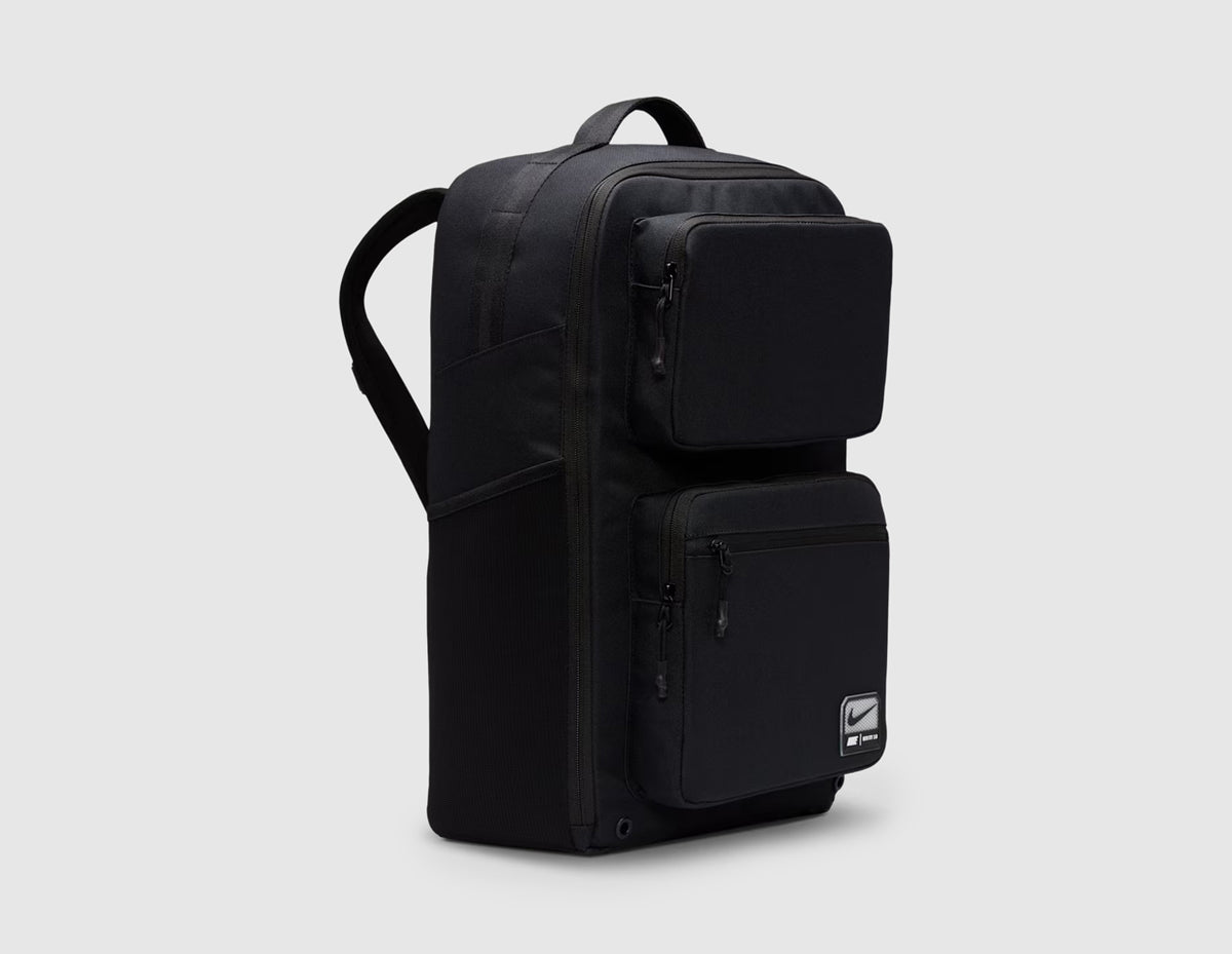 Nike Utility Speed Backpack (27L). Three-quarter view of black training backpack showcasing side profile, dual front zippered utility compartments, and side pocket construction. 