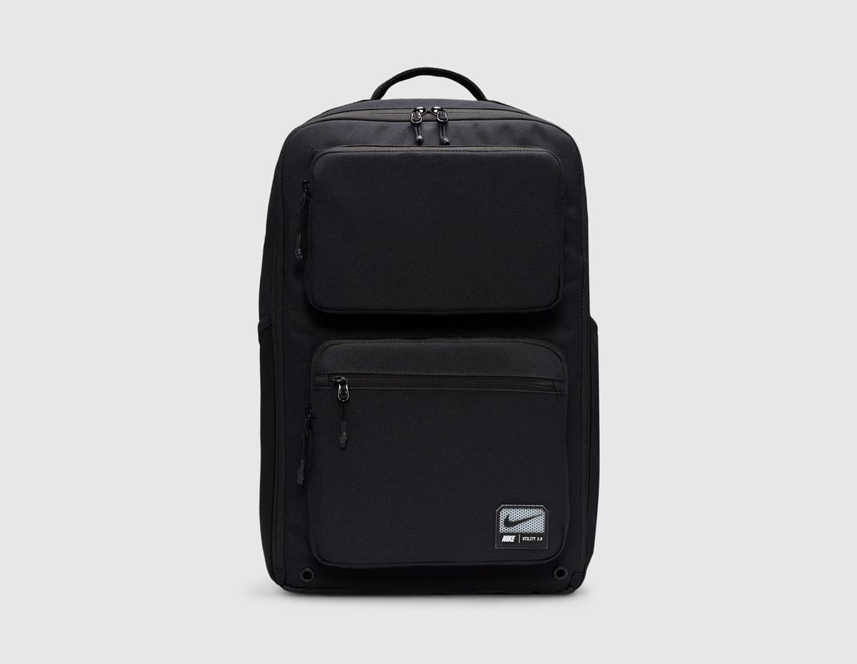Nike Utility Speed Backpack (27L). Front view of black 27L training backpack featuring dual zip-front utility pockets, woven Nike logo patch on the lower front pocket, top grab handle, and full-zip main compartment. 