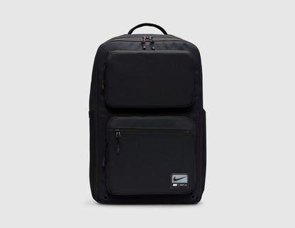Nike Utility Speed Backpack (27L). Front view of black 27L training backpack featuring dual zip-front utility pockets, woven Nike logo patch on the lower front pocket, top grab handle, and full-zip main compartment. 