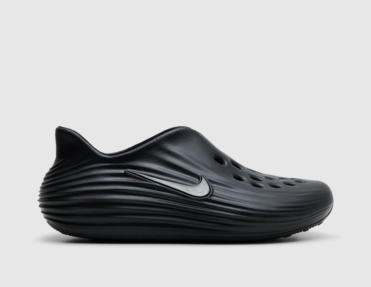 Nike ReactX Rejuven8. Side view of black molded foam slip-on shoes with silver Nike Swoosh logo and sculpted wave texture. 