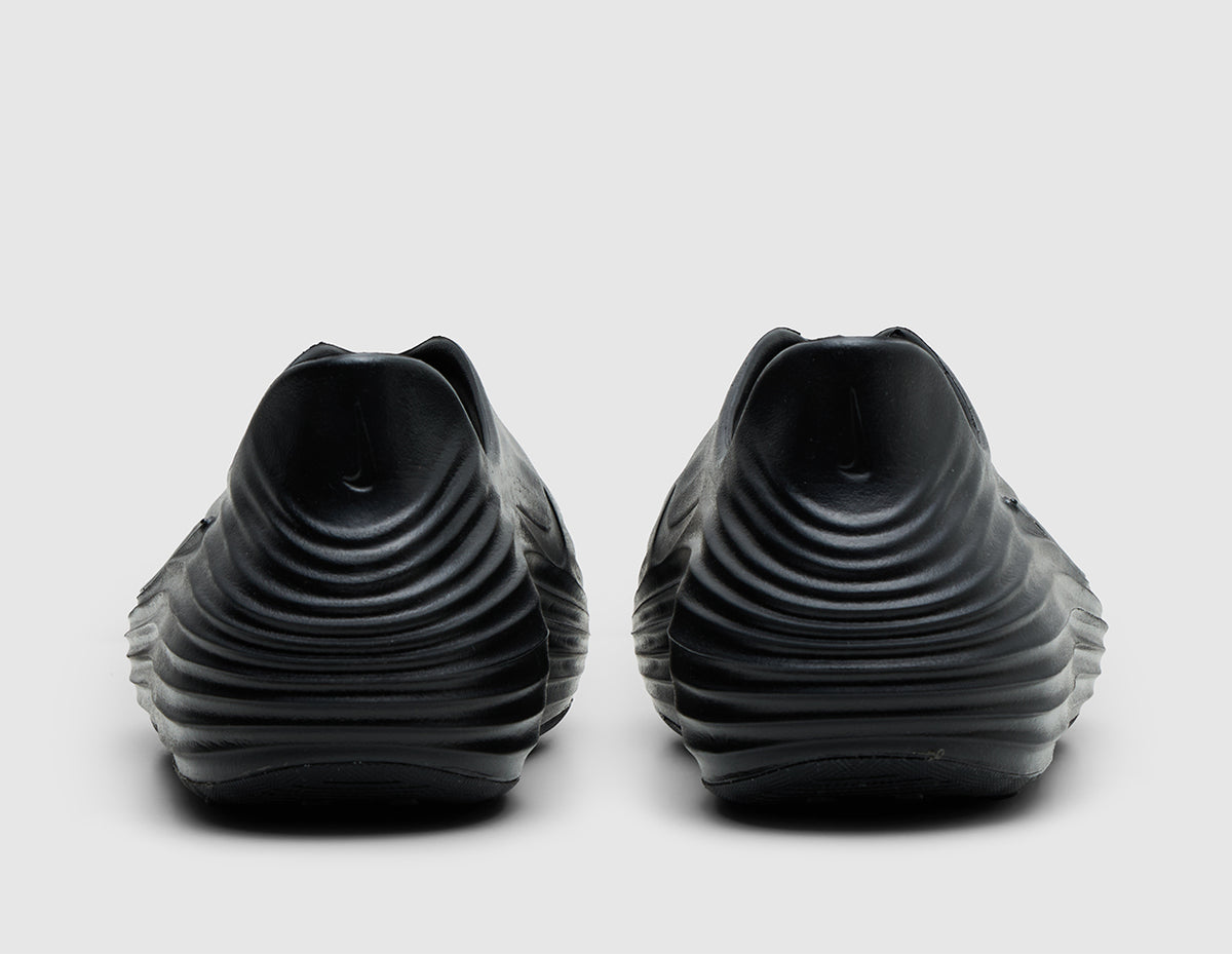 Nike ReactX Rejuven8. Rear view of pair of black molded foam slip-on shoes showing raised heel collars and textured grooves. 