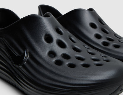 Nike ReactX Rejuven8. Close-up of black molded foam slip-on shoes showing toe box ventilation cutouts and side wave texture. 