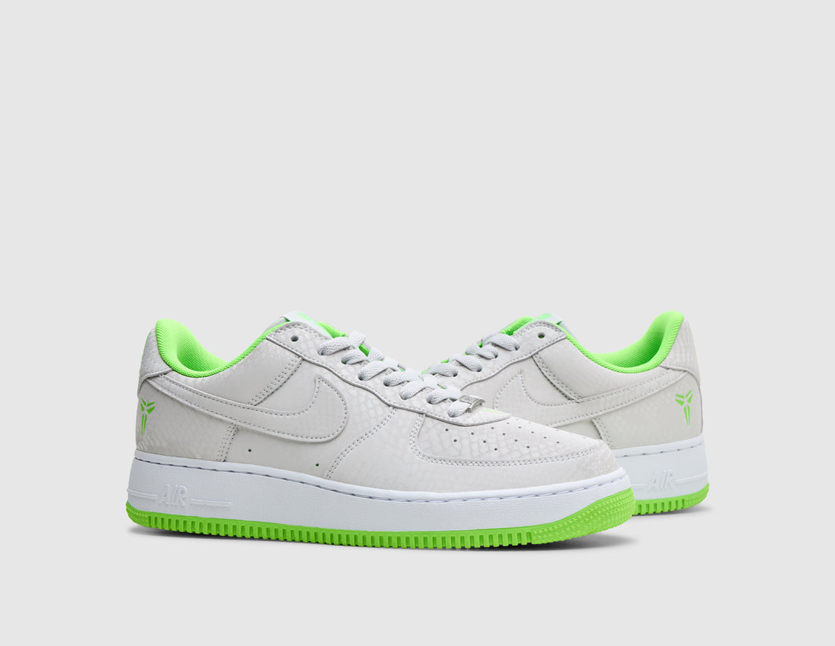 Nike Kobe Air Force 1 Low. Three-quarter view of pair of vast grey sneakers showing tonal leather Swoosh, vast grey laces, electric green inner lining, and white soles. 