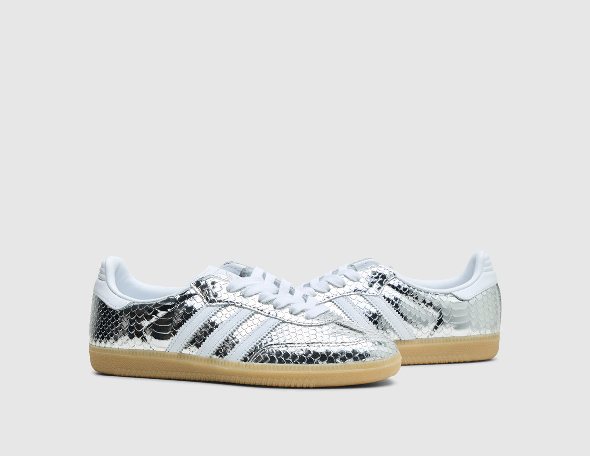 adidas Women's Samba. Three-quarter view of pair of silver metallic snakeskin sneakers showing white Three Stripes, white laces, and low-profile gum rubber soles. 