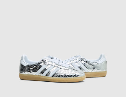 adidas Women's Samba. Three-quarter view of pair of silver metallic snakeskin sneakers showing white Three Stripes, white laces, and low-profile gum rubber soles. 