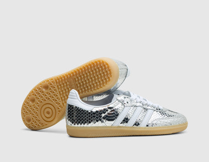 adidas Women's Samba. Three-quarter view of silver metallic snakeskin sneakers with one shoe turned to showcase the low-profile gum rubber outsole. 