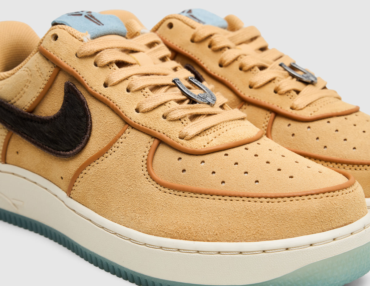 Nike Kobe Air Force 1 Low Protro. Close-up three-quarter view of the upper showing perforated twine suede toe box, flax laces with horseshoe lace dubrae, light blue tongue tab with black Kobe Sheath logo, and baroque brown ponyhair side Swoosh. 