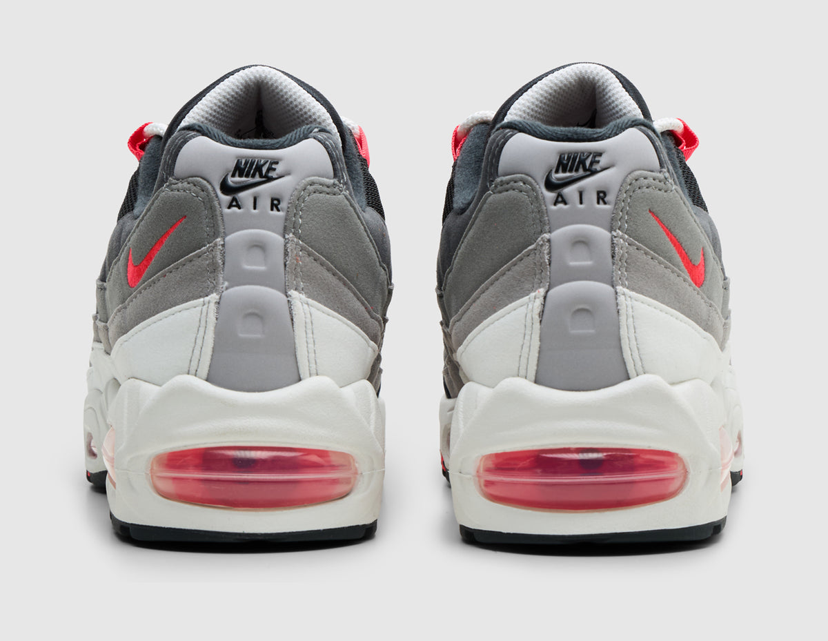 Nike Air Max 95 OG Big Bubble. Rear view of pair of reverse grey and anthracite gradient sneakers showing light grey heel tabs with black Nike Air logos, solar red mini Swooshes, and large solar red Air cushioning units. 