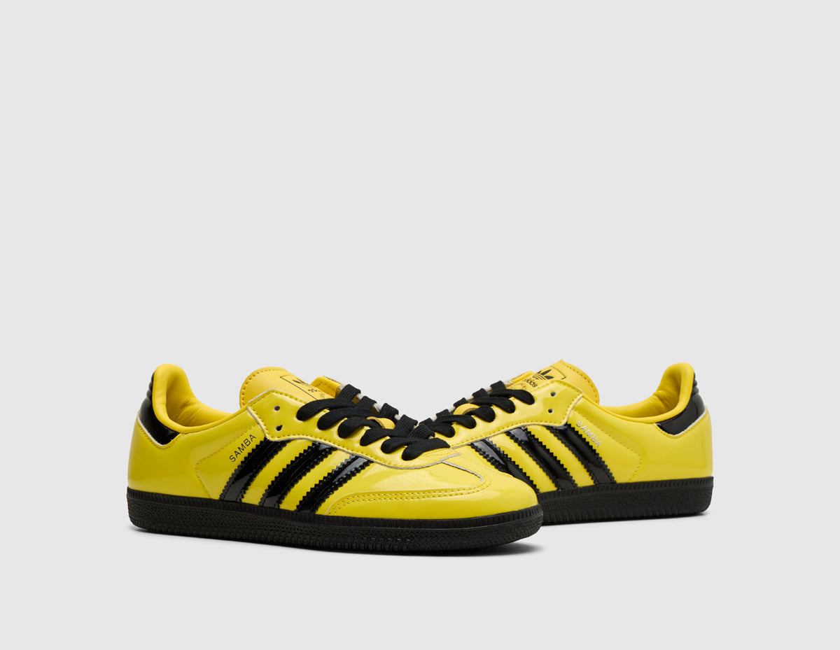 adidas Originals Samba OG. Three-quarter view of pair of yellow leather sneakers showing black three-stripes, black laces, and yellow T-toe detail. 