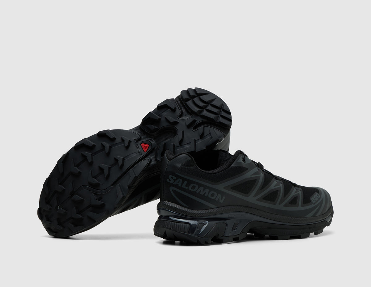 Salomon XT-6. Side view of stacked triple black trail running shoes showing black Contagrip lugged rubber outsole pattern. 