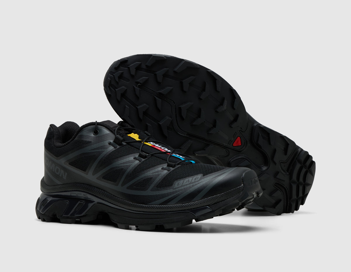 Salomon XT-6. Three-quarter view of triple black trail running shoes with one shoe turned to showcase the lugged rubber outsole. 