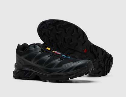 Salomon XT-6. Three-quarter view of triple black trail running shoes with one shoe turned to showcase the lugged rubber outsole. 