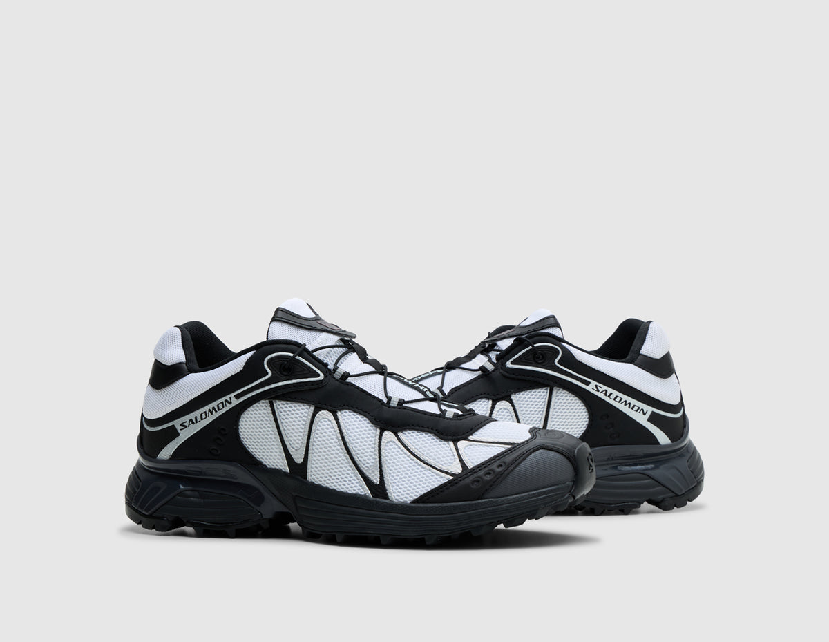 Salomon XT-Whisper. Three-quarter view of pair of black and white trail running shoes showing black overlay webbing, white tongue details, and lugged rubber sole. 