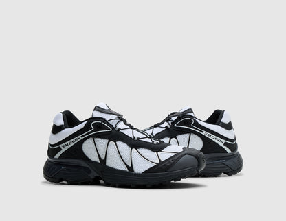Salomon XT-Whisper. Three-quarter view of pair of black and white trail running shoes showing black overlay webbing, white tongue details, and lugged rubber sole. 