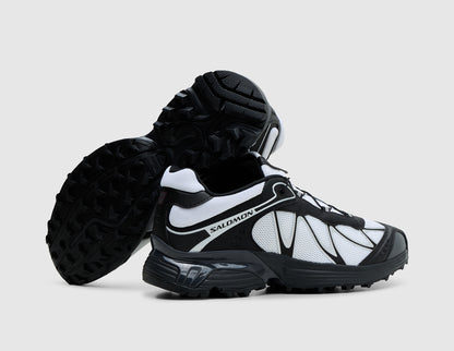 Salomon XT-Whisper. Side view of stacked black and white trail running shoes showing white side panels, black synthetic overlays, and dark rubber outsole tread pattern. 