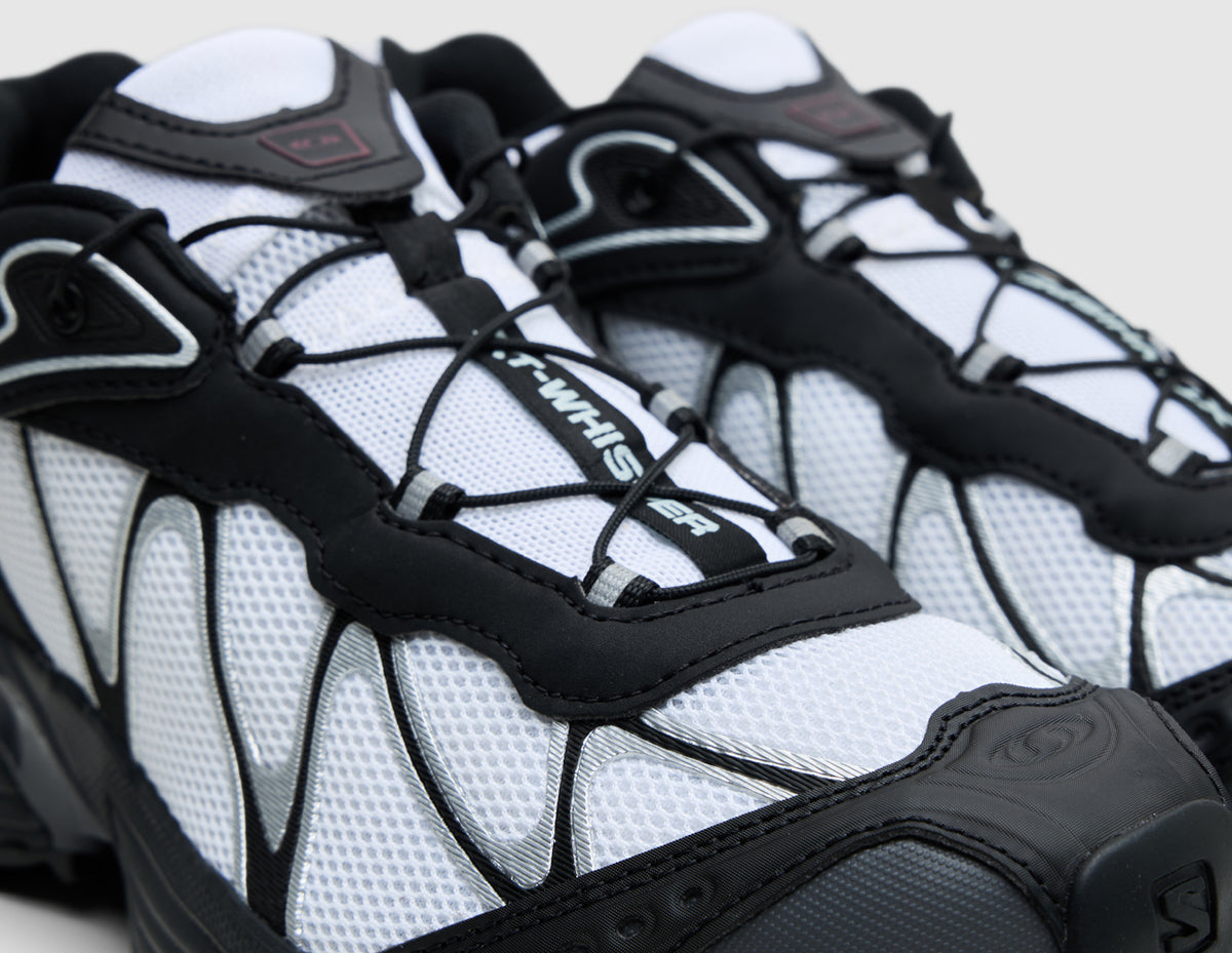 Salomon XT-Whisper. Close-up three-quarter view of white upper showing black webbed overlay cage, Quicklace lacing system, and black toe cap reinforcement. 