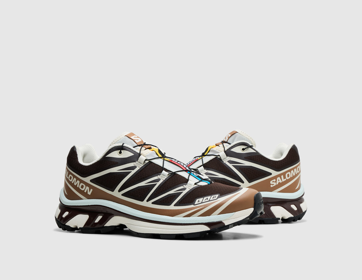 Salomon XT-6. Three-quarter view of pair of black coffee trail running shoes showing burro TPU overlays, Quicklace lacing system with colorful tongue tag, and lugged outsole. 