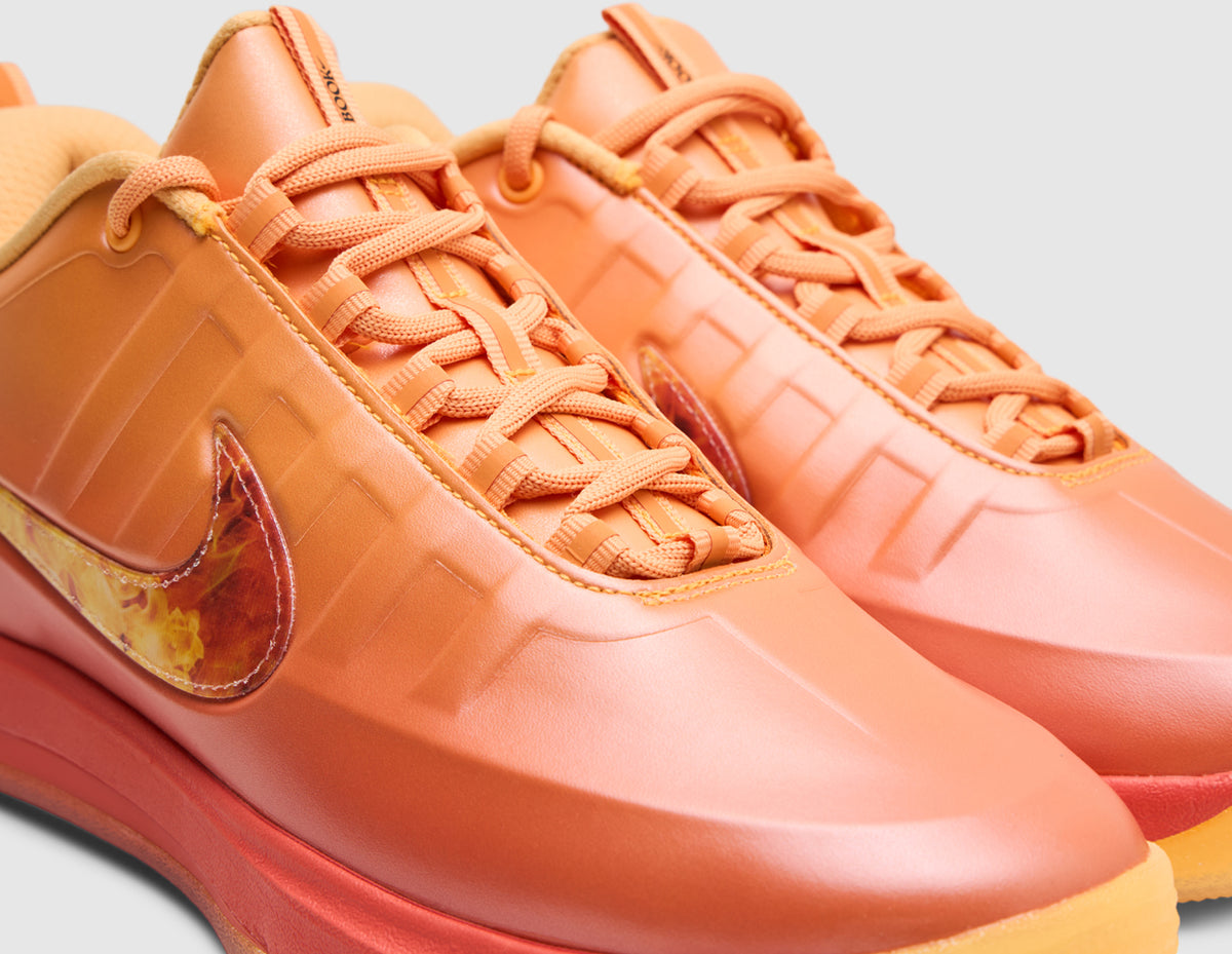 Nike Book 2 "The Phoenix". Close-up three-quarter view of sundial orange upper showing synthetic midfoot ribbing, round sundial laces, tongue pull tab, and flame-graphic Swoosh logo. 