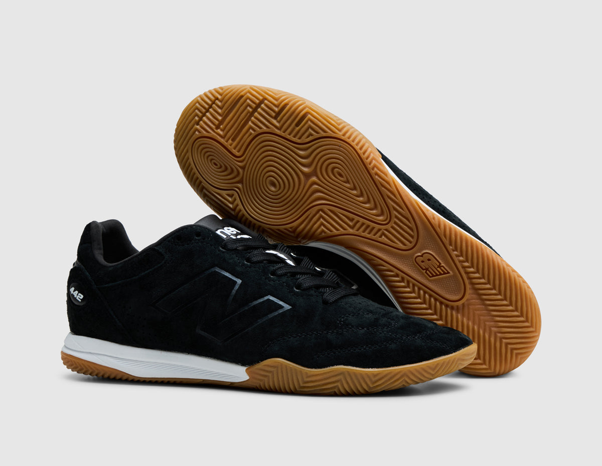 New Balance 442 Elite IN LS V3. Three-quarter view of black sneakers with one shoe turned to showcase the gum rubber outsole. 