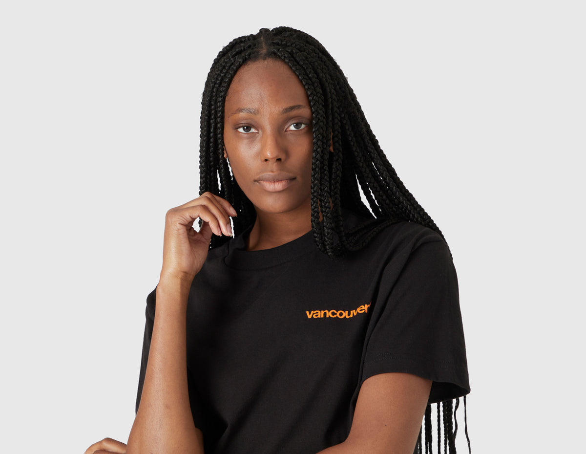 size? Vancouver Logo T-Shirt. Half-length portrait model view of female model wearing the black t-shirt with orange chest logo. 