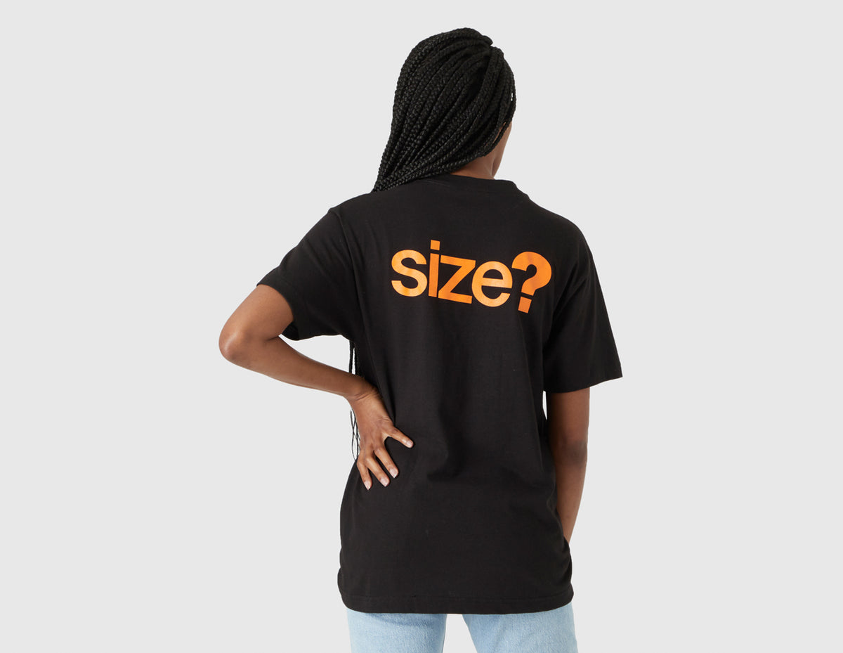 size? Vancouver Logo T-Shirt. Rear model view of female model showing large orange printed "size?" logo graphic across the upper back of the black t-shirt. 